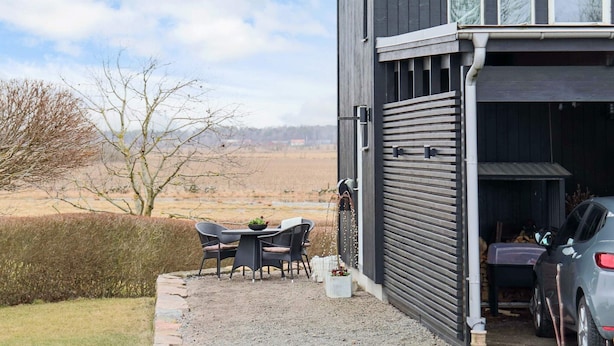 A modern house with a gravel patio, a dining table with chairs, and a car parked in the garage. - 4 Person Holiday Home in Tvaaker (Tvaaker)