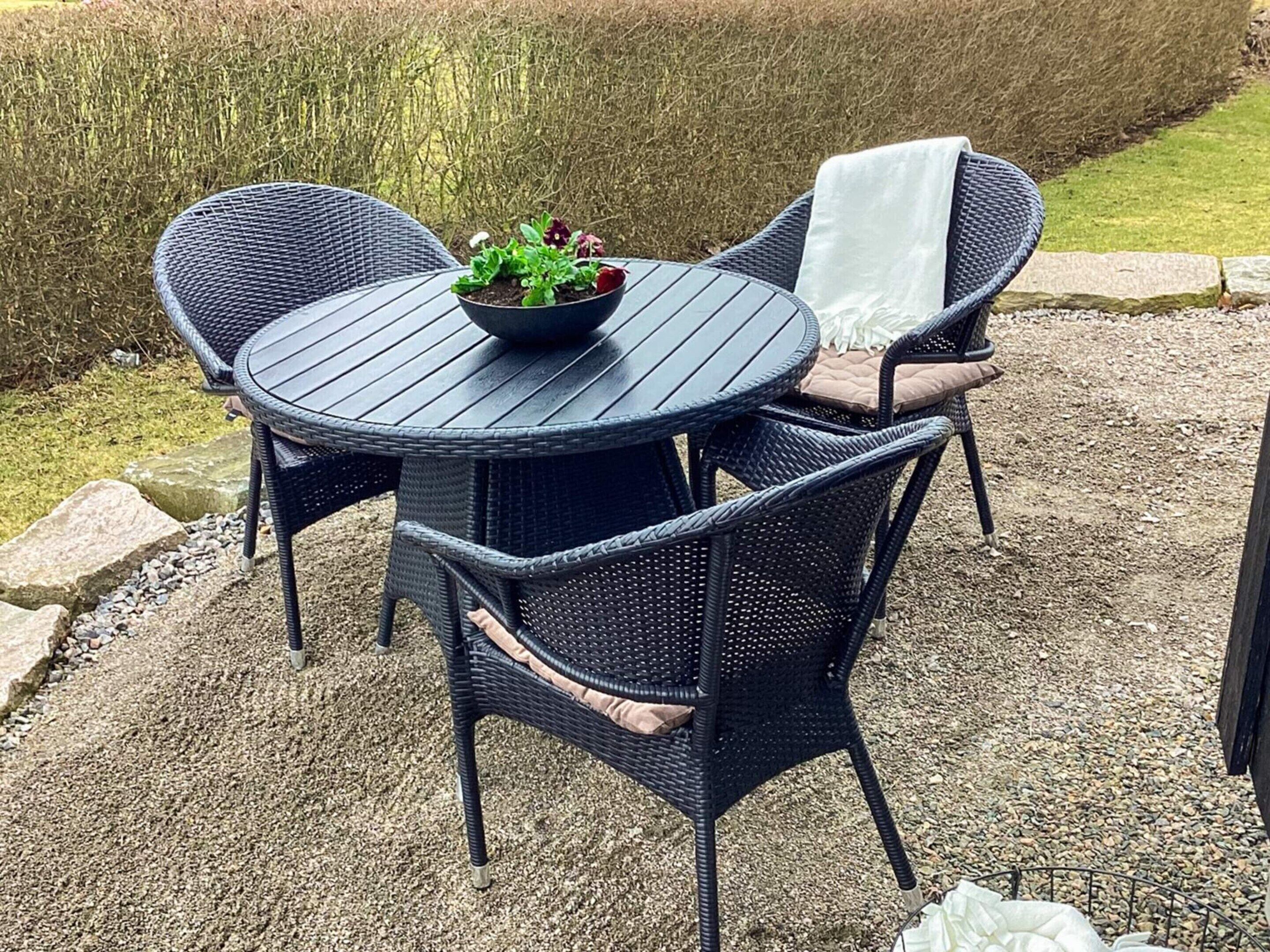 A round outdoor table with wicker chairs, a bowl of plants, and a white cloth on one chair.