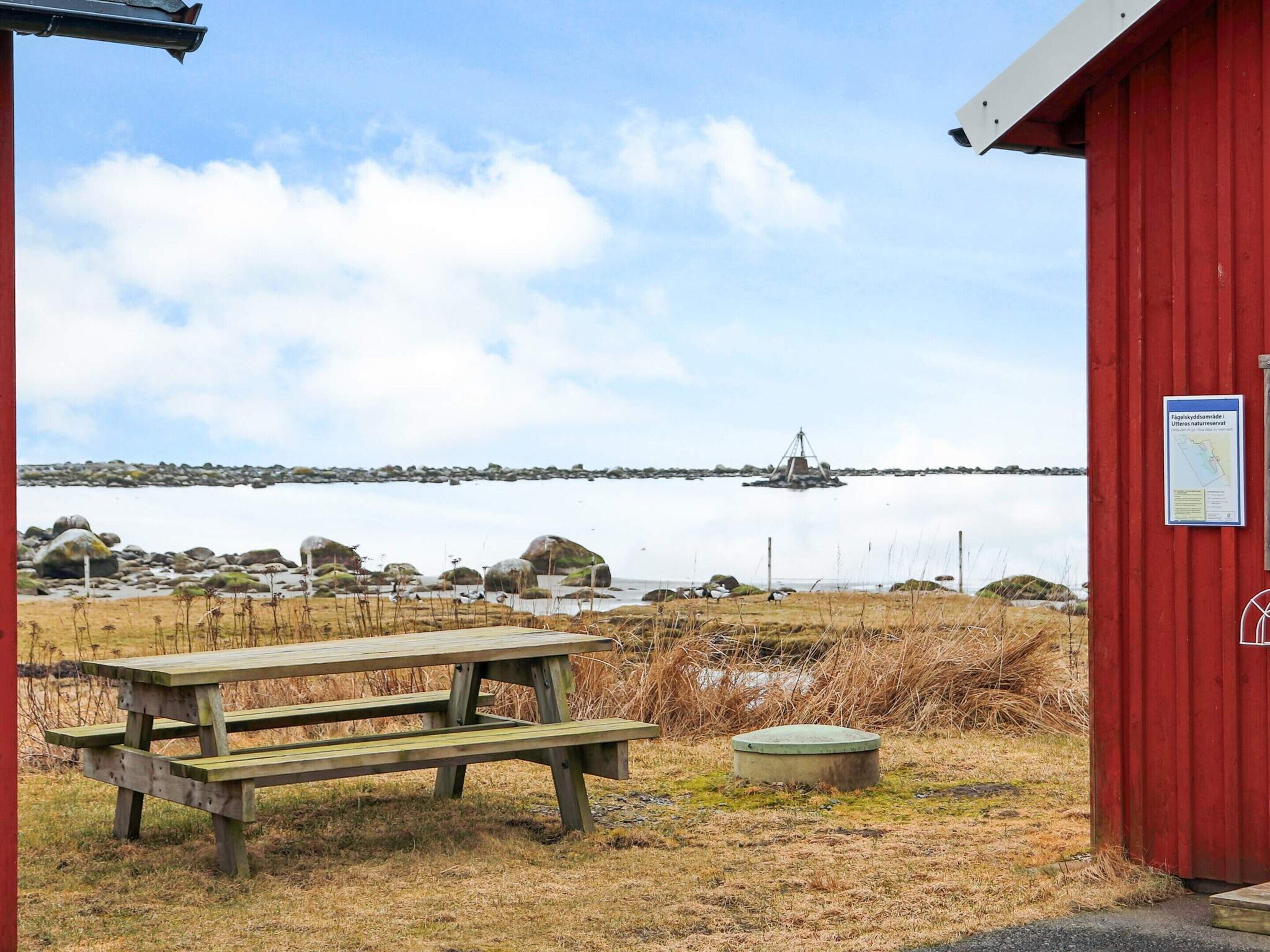 A red building with a picnic table and a small green container nearby.
