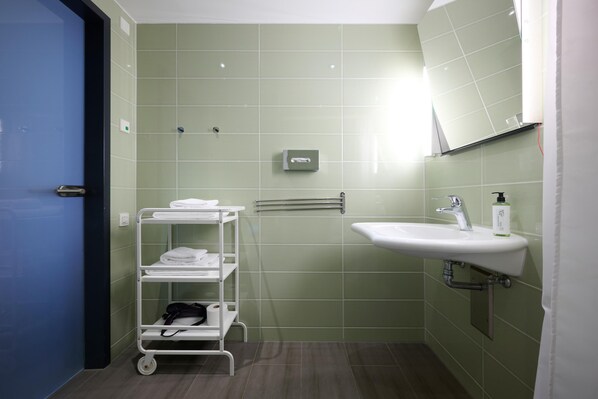 Une salle de bain avec des carreaux verts, un lavabo blanc, un miroir, un porte-serviettes et un chariot contenant des serviettes.