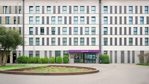 Un hotel de varios pisos con fachada plana, grandes ventanales y un área frontal ajardinada.