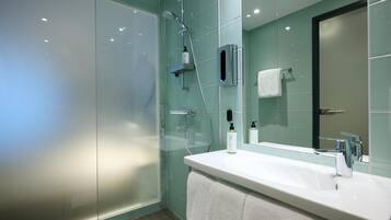 Une salle de bain moderne avec une douche à l’italienne en verre, un lavabo blanc et un miroir.