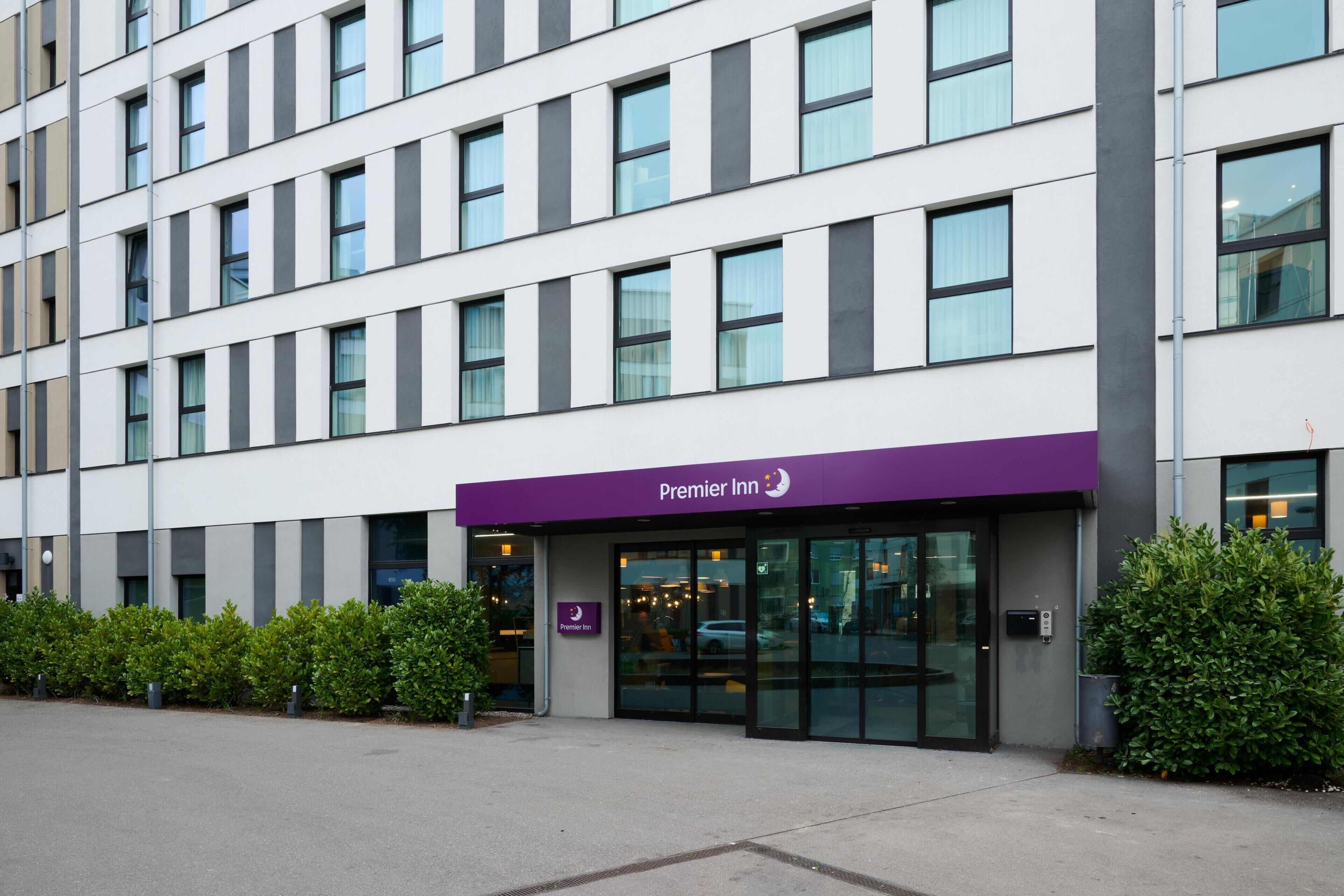 A modern hotel with a flat facade, large windows, and a purple awning.