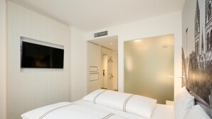 Una habitación de hotel con una cama grande, un televisor de pantalla plana en la pared y un espejo amplio.