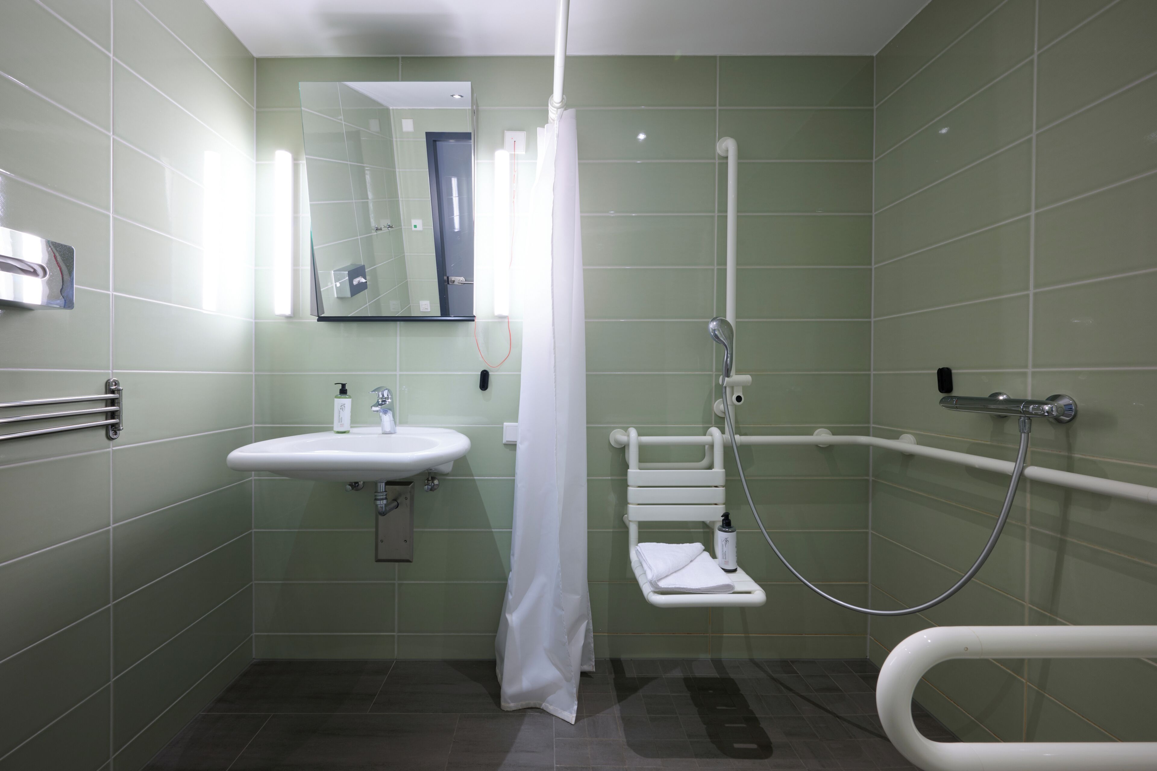 A bathroom with a sink, mirror, shower, and grab bar.