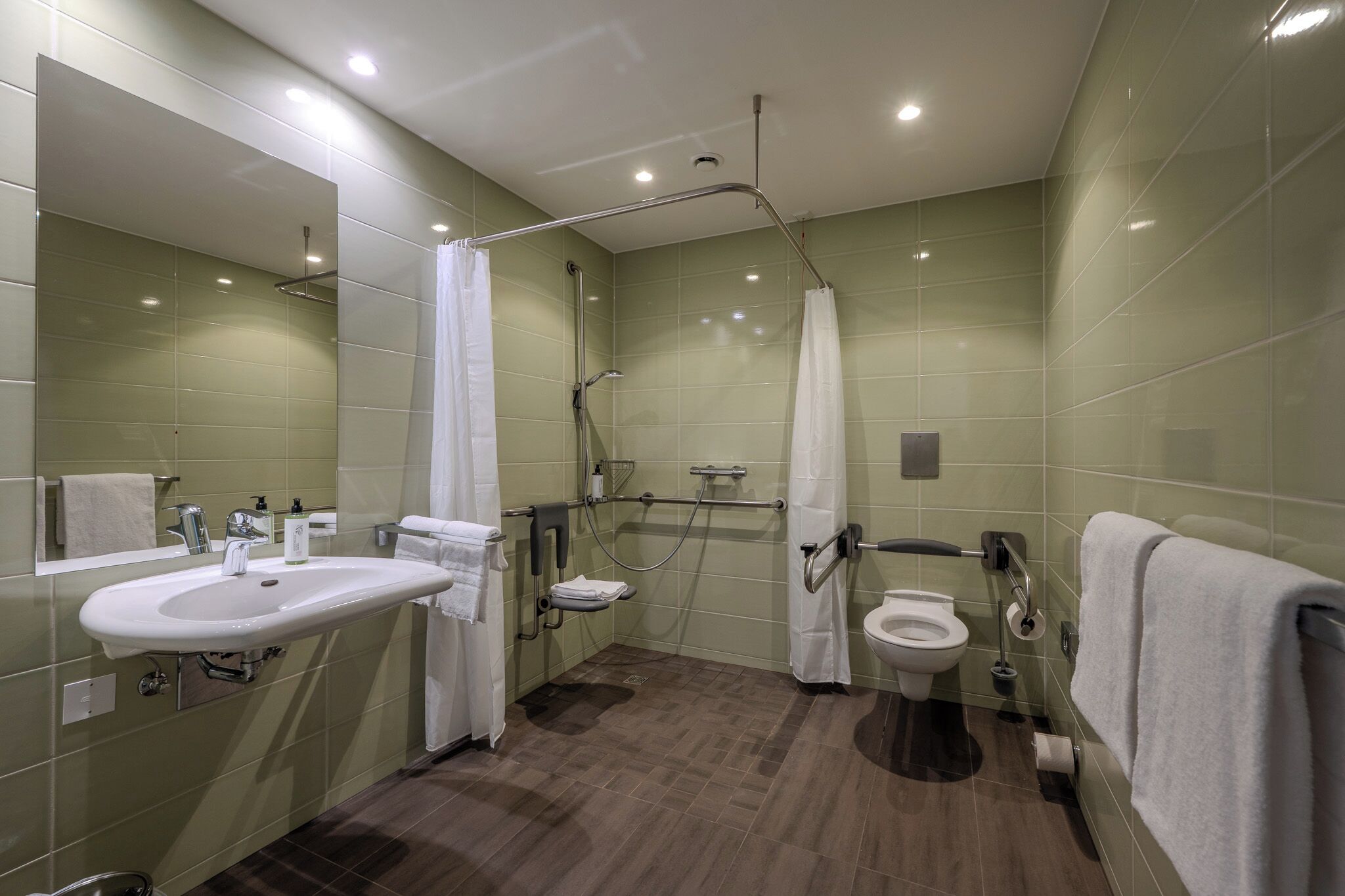 A modern bathroom with a sink, toilet, and shower area, equipped with grab bars and a handrail.