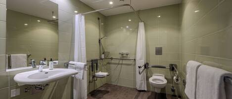 Ein modernes Badezimmer mit Waschbecken, Toilette und Duschbereich, ausgestattet mit Haltegriffen und einer Handstange.
