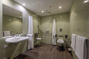 Un baño moderno con lavamanos, inodoro y zona de ducha, equipado con barras de apoyo y pasamanos.