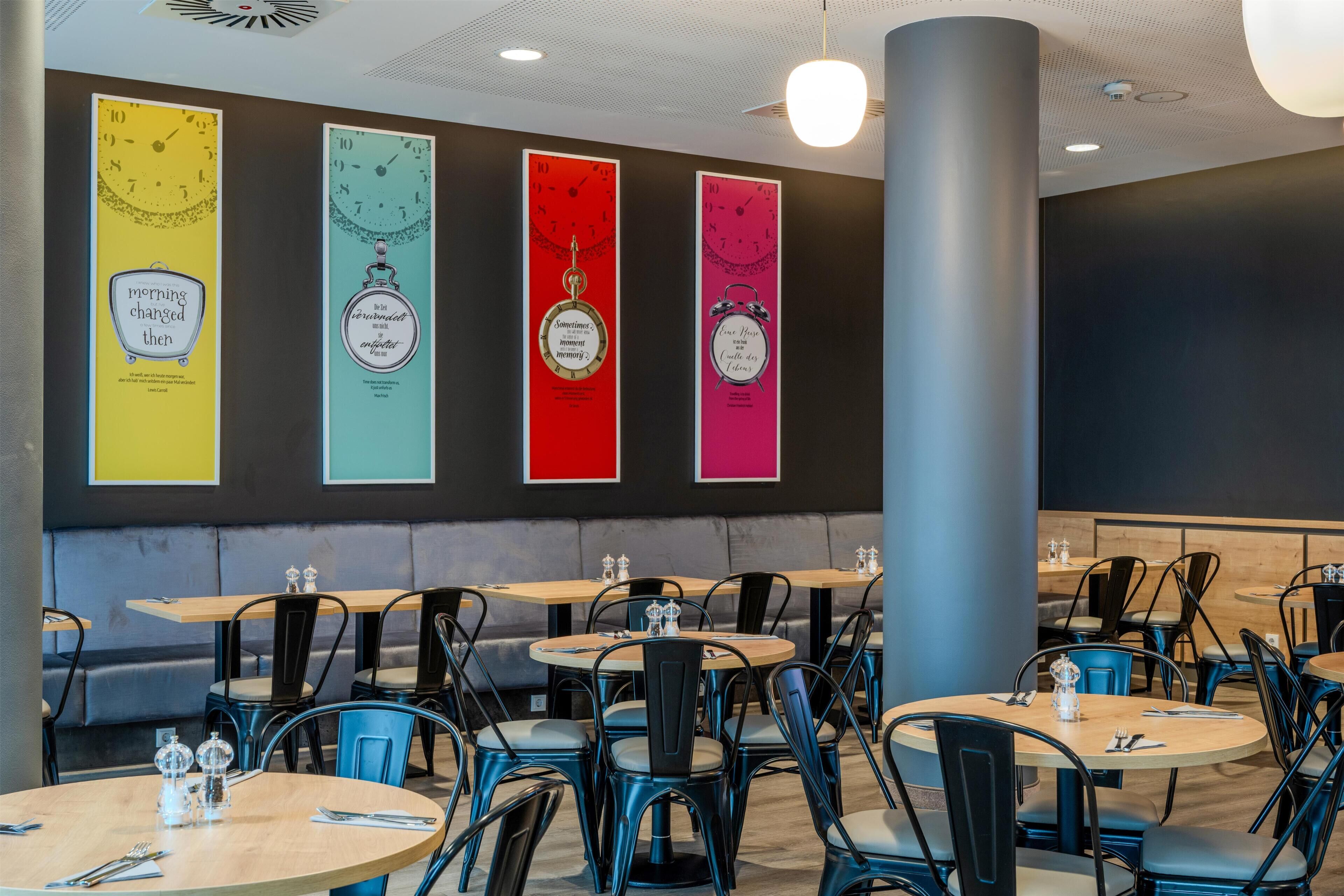 A restaurant interior with round tables, blue chairs, and a wall with colorful vertical banners.