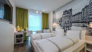 A hotel room with a bed, desk, and a large cityscape mural on the wall.