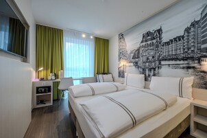 Ein Hotelzimmer mit Bett, Schreibtisch und einem großflächigen Stadtbild-Wandgemälde.