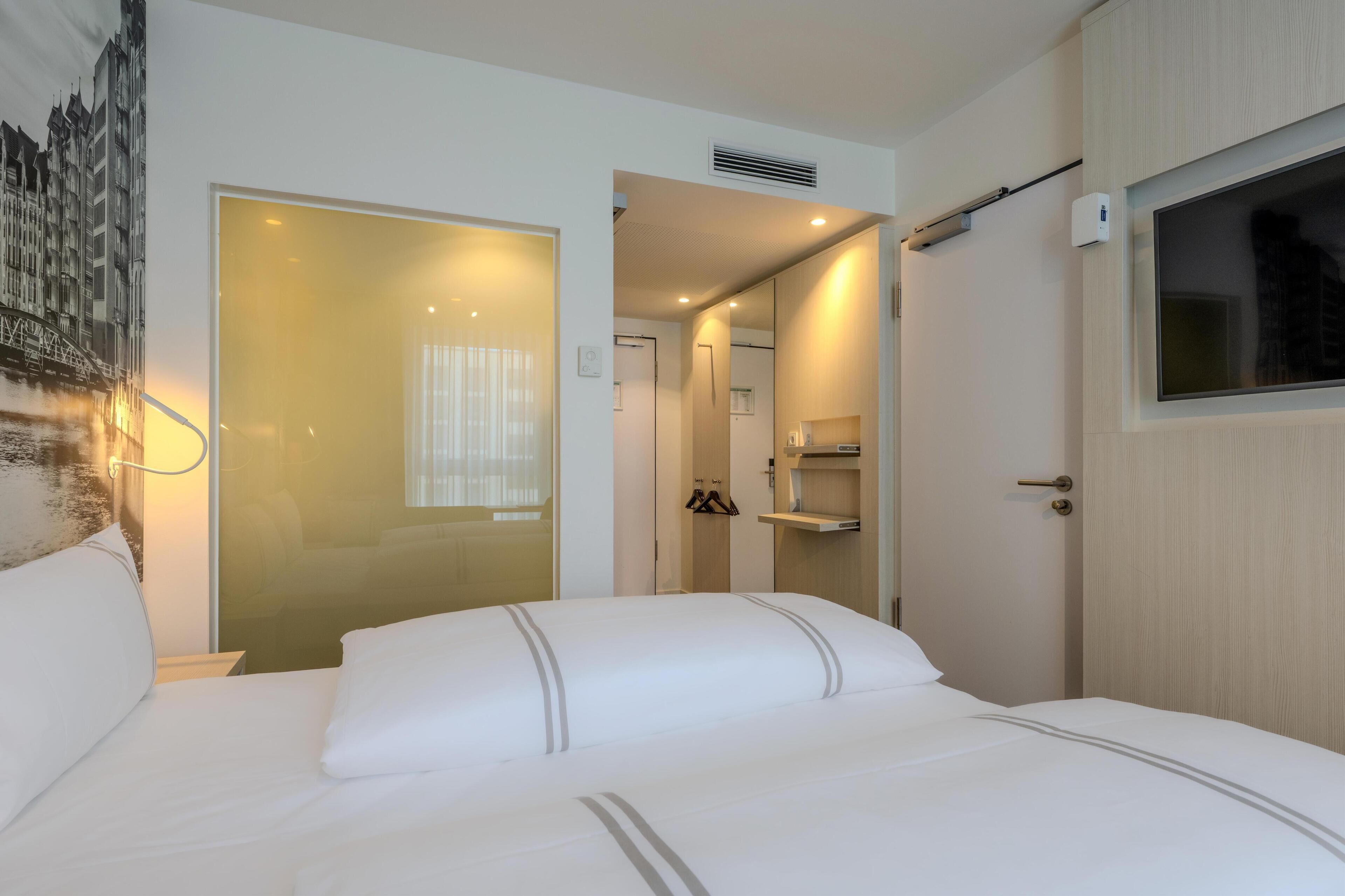 Habitación de hotel con una cama grande, un armario, un espejo, perchero y televisor montado en la pared.