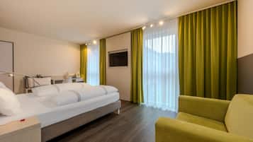 A hotel room with a bed, a desk, a chair, a TV, and curtains.