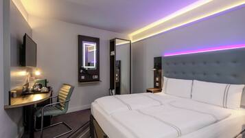 Une chambre d’hôtel équipée d’un lit, d’un bureau, d’une chaise, d’un miroir et d’un téléviseur fixé au mur.