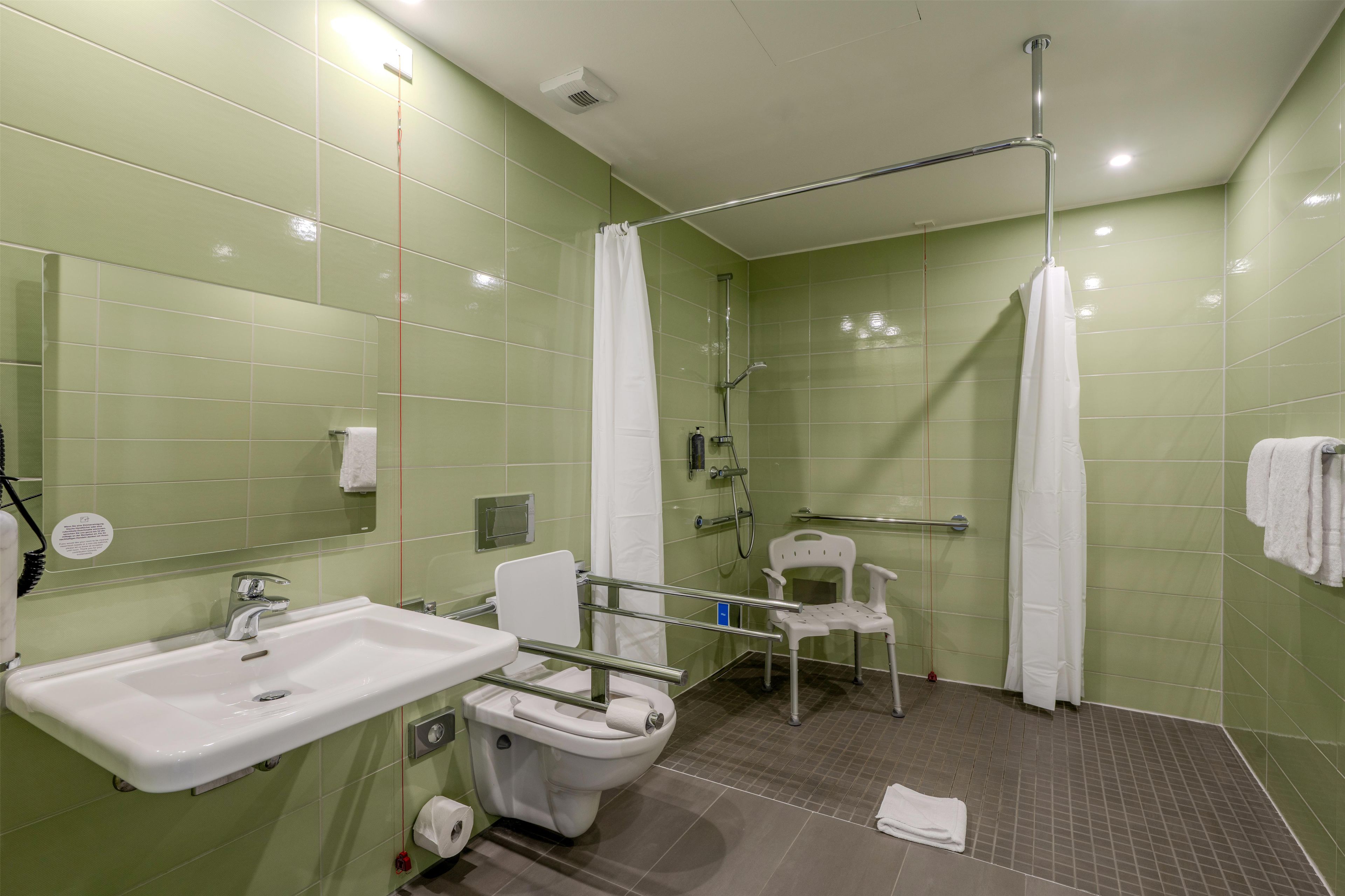 A bathroom with a sink, toilet, shower, and a wheelchair-accessible chair.
