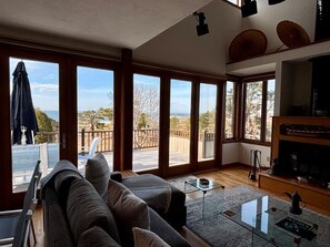 Ett rymligt vardagsrum med stora fönster, en soffa, ett soffbord i glas och en öppen spis.