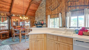 A cabin interior with wooden floors, a stone wall, a kitchen with wooden cabinets, and a dining area with chairs and a table. - Almond Family Retreat (Almond)