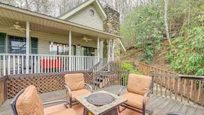 A covered outdoor deck with two cushioned chairs, a stone table, and a wooden staircase leading to a porch. - Almond Family Retreat (Almond)