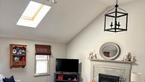 A living room with a fireplace, a television, a sofa, a coffee table, and a bookshelf. - Short Drive to Red River Beach (Harwich)