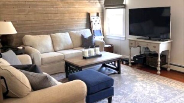 A living room with a sofa, ottoman, coffee table, TV stand, and a patterned rug. - Short Drive to Red River Beach (Harwich)
