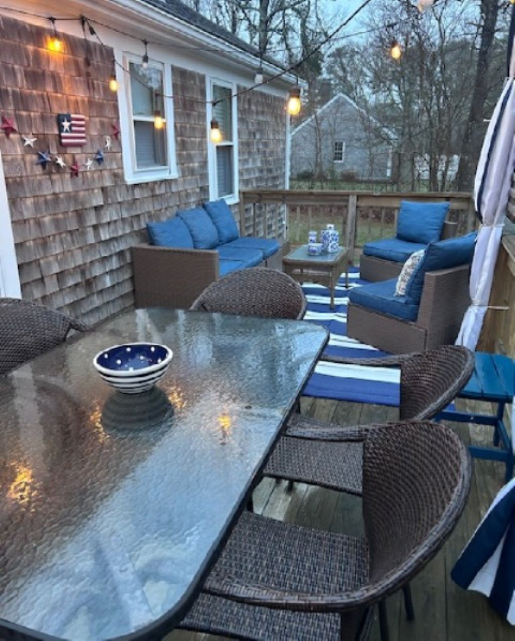 Eine Terrasse im Freien mit einem Glastisch, Korbmöbeln und blauen Kissen.