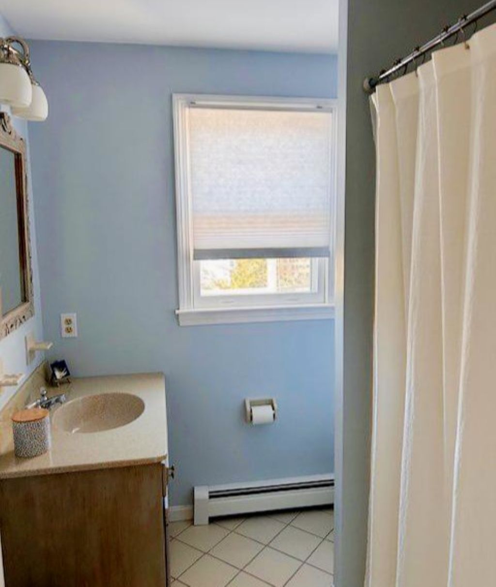 A bathroom with a sink, window, and shower curtain.
