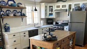 A kitchen with white cabinets, a wooden island, and blue and white dishes on shelves. - Short Drive to Red River Beach (Harwich)