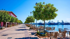 A waterfront promenade with outdoor seating, a row of buildings, and yachts docked in the background. - Seaside Escape With Balcony in Paleo Faliro (Palaio Faliro)