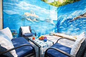 Um pátio com um mural, área de estar externa e uma mesa com frutas e bebidas.