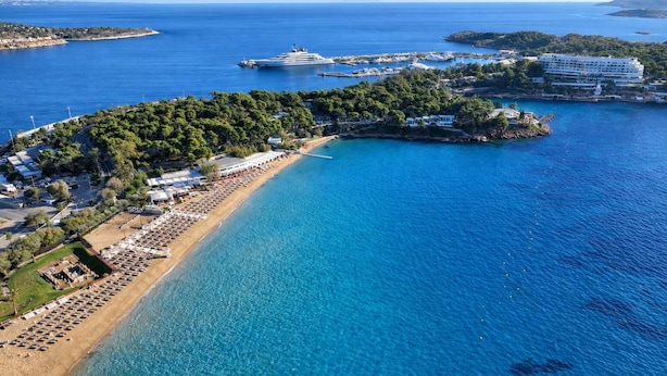 An aerial view of a coastal area with a beach, a cruise ship docked, and a resort with multiple buildings. - Seaside Escape With Balcony in Paleo Faliro (Palaio Faliro)