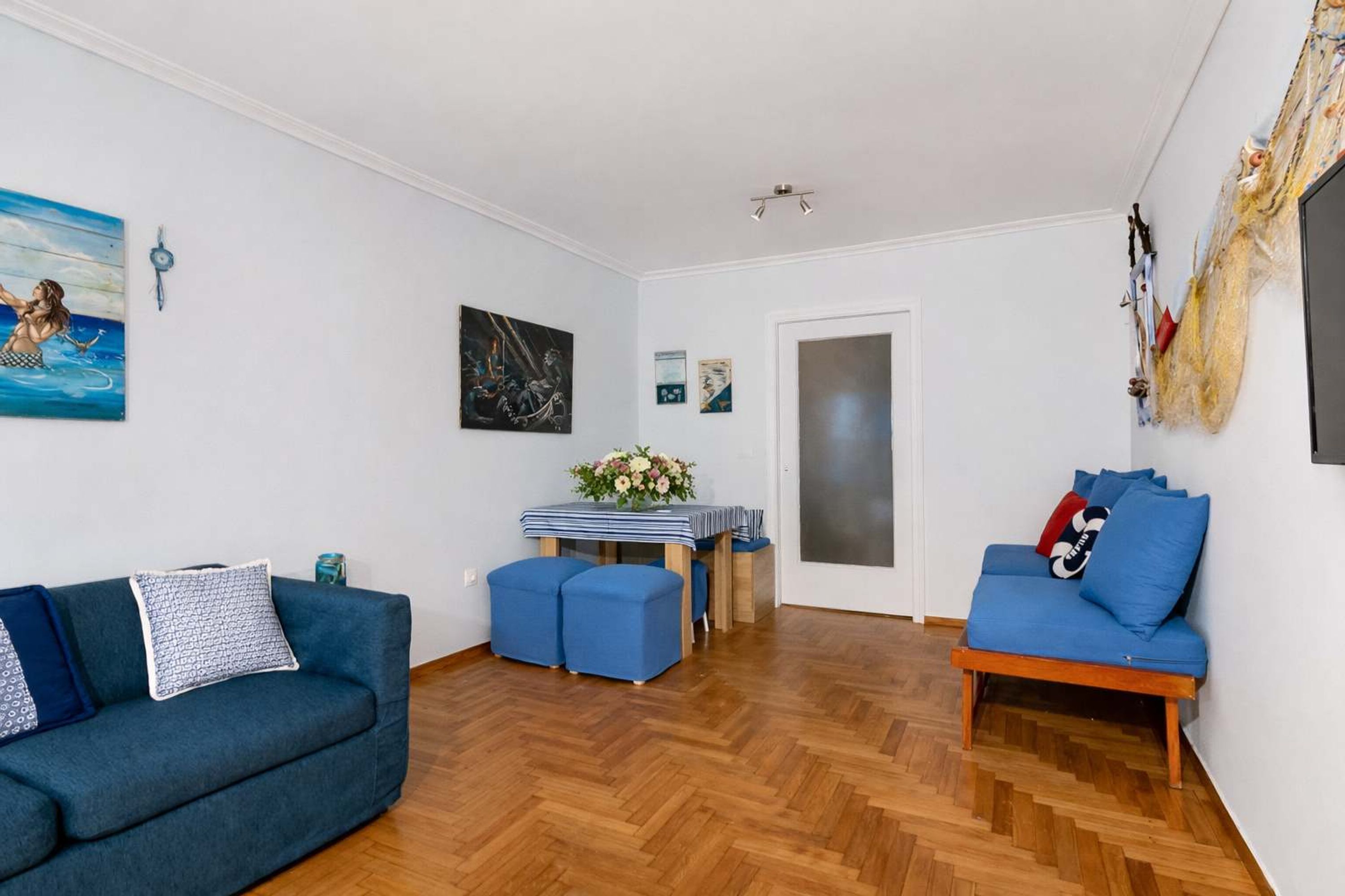 Ein Wohnzimmer mit einer Couch, Poufs, einem Tisch mit Blumen und einer Tür.