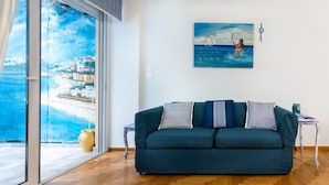 A room with a sofa, a painting, and a view through a glass door. - Seaside Escape With Balcony in Paleo Faliro (Palaio Faliro)