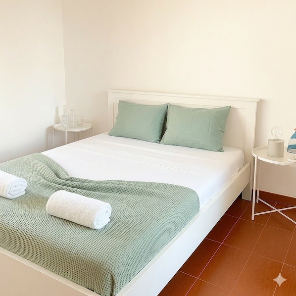 A neatly made bed with a green blanket and pillows, a small bedside table with a lamp, and a glass of water on the nightstand.