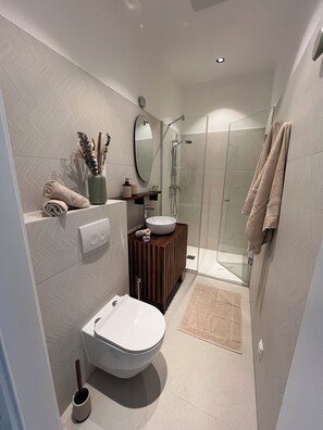 Ein modernes Badezimmer mit Toilette, Waschbecken, Dusche und Spiegel.