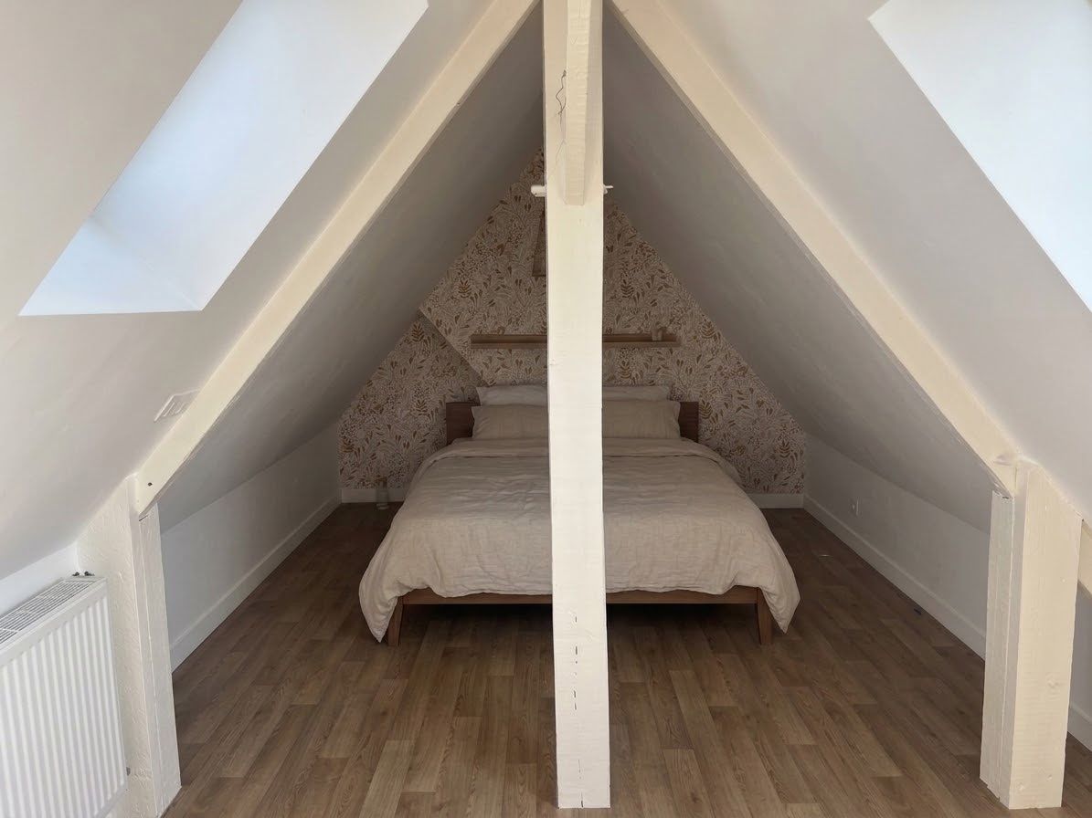 Ein Schlafzimmer mit schrägem Dach, einem Bett und einer Heizkörper.