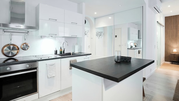 A modern kitchen with white cabinetry, a black countertop, stainless steel appliances, and a large island. - Modernized 1920s Apartment (Turku)