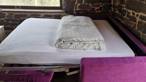 Een bed met een witte lakenset en een bed met een patroon, een paarse bank en een stenen muur.