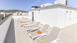 Kattoterassi aurinkotuoleineen, pieni savupiipullinen rakennus ja selkeä näkymä kaupunkimaisemaan taustalla.