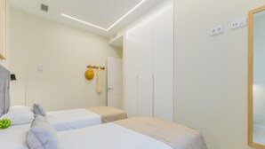 Hotellihuone, jossa on kaksi sänkyä, vaatekaappi, peili ja pieni kasvi.