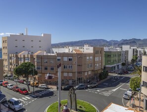 Um edifício de vários andares com um pátio central, uma rua com carros estacionados e vista clara para montanhas distantes.