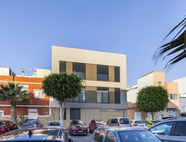 Um edifício moderno com telhado plano, janelas amplas e um estacionamento com diversos carros.