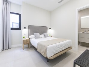 Ein modernes Schlafzimmer mit einem großen Bett, Nachttischlampen, einem kleinen Nachttisch mit einem Buch und einem Fenster mit Vorhängen.