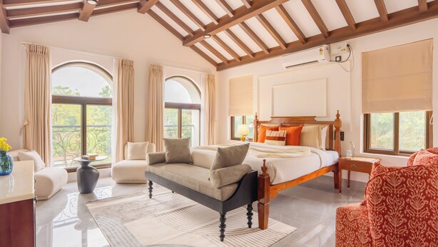A spacious bedroom with a large bed, a sofa, a chair, and a desk. - Elivaas Casa Verdea 4BHK Villa With Pool (Siolim)