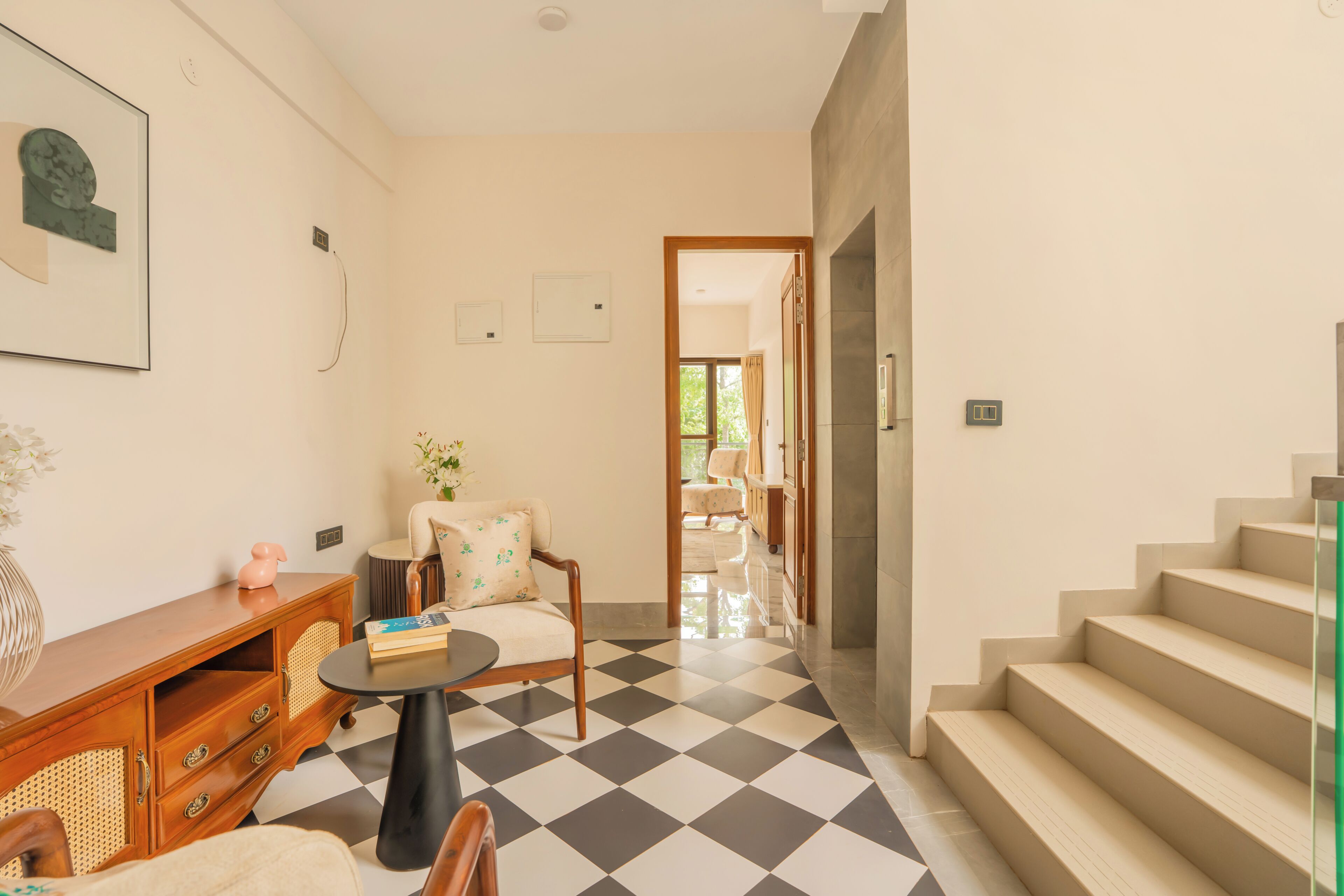 A modern interior with a checkered floor, a staircase, a wooden cabinet, and a chair.