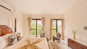 A bedroom with a large bed, a sofa, a small table, and a cabinet. - Elivaas Casa Verdea 4BHK Villa With Pool (Siolim)