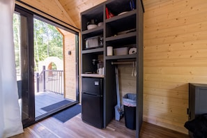 Eine kleine Küche mit Kühlschrank, Regalen und einer Mülltonne.