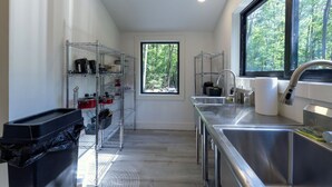 A modern kitchen with stainless steel appliances, a large window with a forest view, and organized shelves. - Glamping at Four Fillies Lodge-The Little John (Peterstown)