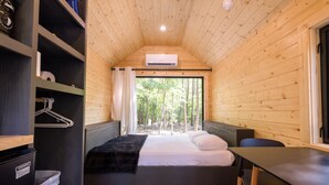 A cabin with a bed, a table, and a window with a forest view. - Glamping at Four Fillies Lodge-The Little John (Peterstown)