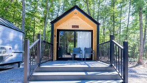 A wooden cabin with a sign reading 'Little John,' a covered outdoor seating area, and a gravel ground. - Glamping at Four Fillies Lodge-The Little John (Peterstown)