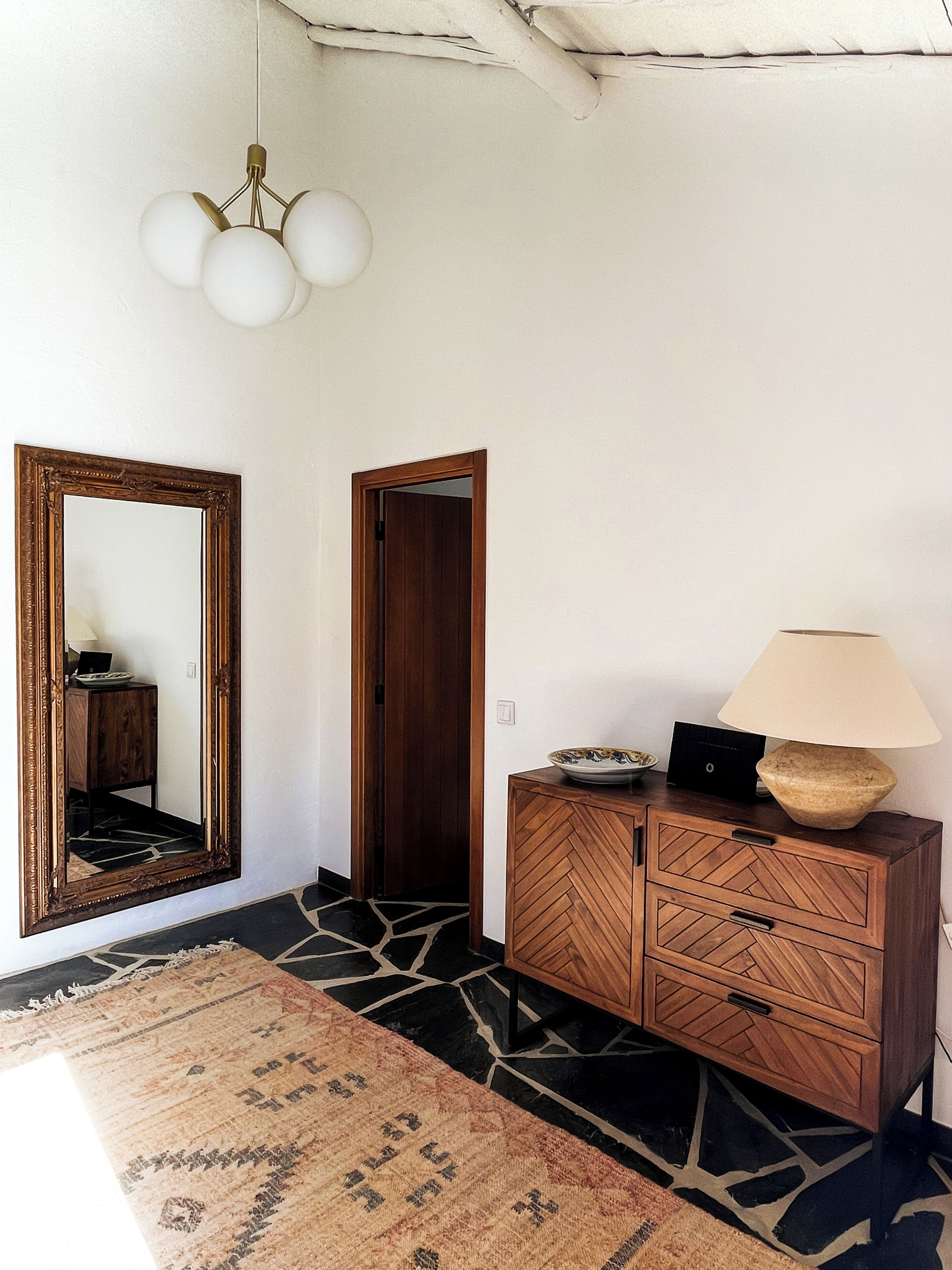 A room with a wooden cabinet, a mirror, a lamp, and a patterned rug.